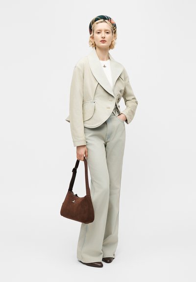 Νεαρή γυναίκα φοράει εκρού σακάκι, παντελόνι φαρδύ, καρό κορδέλα στα μαλλιά, κρατώντας καφέ σουέντ τσάντα χειρός με λουρί ώμου, στέκεται σε λευκό φόντο.
