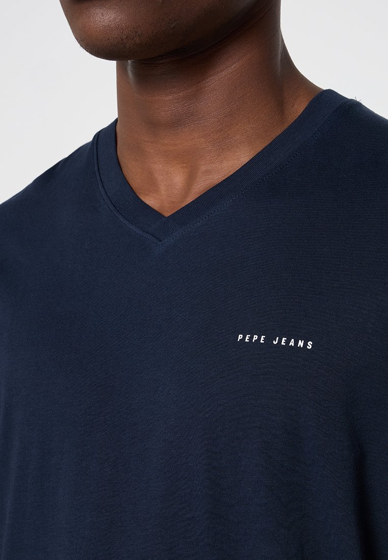 Camiseta de cuello en V azul marino hecha de una tela suave, con un pequeño logo blanco de "PEPE JEANS" en la parte izquierda del pecho. Textura suave.