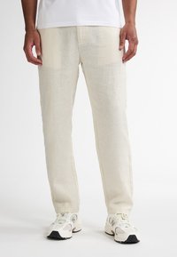 Lys beige lærredsbukser med lige snit, der har en glat tekstur og en subtil glans, parret med hvide atletiske sneakers.