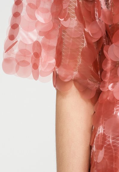 Ροζ δίχτυ ένδυμα διακοσμημένο με διαφανείς κυκλικές παγιέτες, διαθέτοντας στρωματοποιημένη υφή και κρεμαστό σχέδιο που δημιουργεί κίνηση.