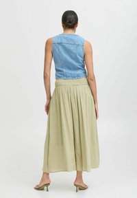 Veste sans manches en denim au design ajusté, associée à une jupe fluide de longueur cheville de couleur vert clair avec une taille élastique.