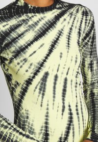 Dlouhý rukáv, vypasovaný top v světle žluté barvě s černým tie-dye vzorem. Má žebrovaný výstřih a strukturovanou tkaninu pro pohodlné nošení.