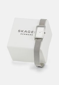 Silverfärgad rektangulär klocka med mesharmband, vit urtavla och minimalistisk design, visad på en vit låda med "SKAGEN DANMARK" tryckt.