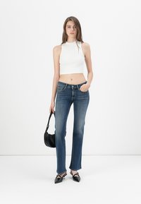 Weißes, tailliertes Crop-Top. Dunkelblaue, gerade geschnittene Denim-Jeans. Schwarze Handtasche mit Schultergurt. Schwarze spitze Absätze mit Knöchelriemen.