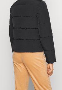 Czarna kurtka puchowa z poziomymi przeszyciami, teksturowany materiał i krótki fason. W połączeniu z jasnobeżowymi spodniami z korduroju.