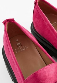 Pantofi slip-on din suede roz, cu vârf rotund și talpă joasă neagră. Interiorul prezintă căptușeală din piele maro, cu logo embosat.