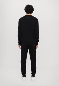 Felpa nera e pantaloni abbinati, entrambi con una texture liscia. Caratteristiche includono polsini e orlo a coste; accentuazione del logo cucito sui pantaloni.