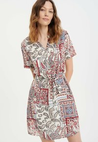 Korte mouwen jurk met een mix van paisley- en geometrische patronen in rood, blauw en crème. Knopsluiting aan de voorkant en verstelbare strik taille.