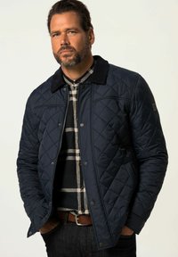 Námořnická prošívaná bunda s kordovou límcem, předními patentkami a diamantovým vzorem. Nosičná přes černou a šedou kostkovanou košili.