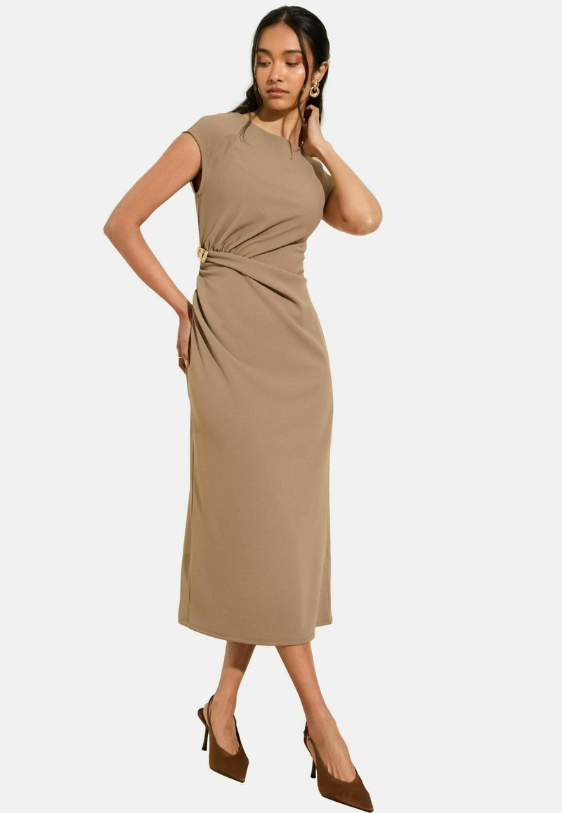 Midi-jurk in een zachte beige stof met korte mouwen,Gathered op de taille met een gouden accent. Gecombineerd met bruine hoge hakken.