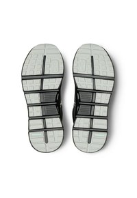 Des chaussures de sport noires avec une semelle grise flexible et texturée. Le dessous présente un motif en grille avec des rainures proéminentes pour une meilleure adhérence.