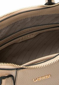 Interno di borsa in pelle beige strutturata con tasche con cerniera, accessori in tonalità oro e fodera decorata con un motivo a logo sottile.