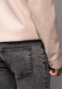 Suéter de forro polar beige con costuras redondeadas en los hombros, combinado con jeans de mezclilla grises que cuentan con un bolsillo trasero y un detalle de botón visible.