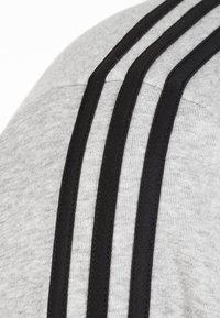 Tessuto di felpa grigia con tre strisce nere verticali lungo la cucitura della spalla, che mostra una consistenza morbida e un design sportivo.