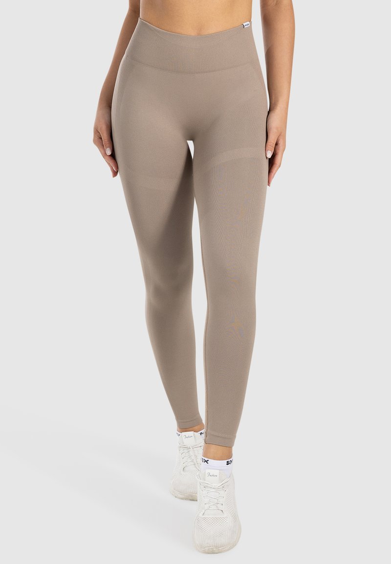 Licht beige leggings met een hoge tailleband, gestructureerde stof, gladde afwerking en subtiele accentdetails langs de zijkanten.