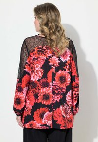 Blommig långärmad blus med svarta spetsdetaljer. Har livfulla röda och rosa blommönster på en svart bakgrund. Lös passform.