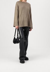 Beige oversized tröja med ribbad nederkant, i kombination med svarta faux läder byxor. Modellen håller en liten svart handväska. Släta texturer genomgående.