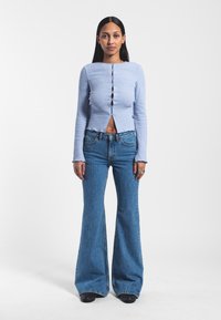 Light blue ribbed long-sleeve top with buttons down the front, paired with high-waisted flared blue jeans, featuring a raw hem.