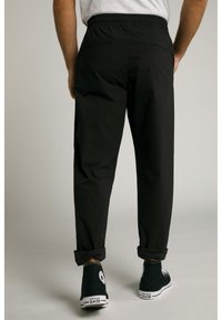 Pantalones negros de cintura elástica con un ajuste cónico, que presentan dos bolsillos traseros y los puños enrollados, combinados con zapatillas de lona negras.