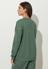 Sudadera verde hecha de una suave mezcla de algodón, con un escote redondo, hombros caídos y puños acanalados. Diseño sencillo y de corte relajado.