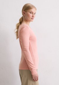 Helles rosa Langarmshirt mit runder Ausschnittform und Seitennähten. Weicher, strukturierter Stoff mit figurbetontem Design, kombiniert mit beigen Hosen.
