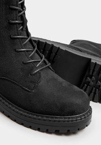 Stivali neri alla caviglia in suede, con un design metallico per la chiusura a lacci, suola in gomma robusta con un motivo testurizzato e cuciture rinforzate.