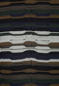 Neulottu kangas, jossa vuorottelevat vaakasuorat raidat tummanvihreässä, mustassa, ruskeassa, laivastonsinisessä ja valkoisessa; vaihteleva paksuus luo teksturoidun ilmeen.