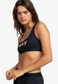 Marine sportbeha met een ronde halslijn en brede banden. Voorzien van een opvallend beige "roxy" logo aan de voorkant en zwarte taillebandaccenten.