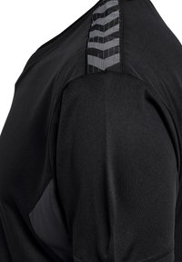 Camiseta deportiva negra con un diseño texturizado en el hombro, hecha de un tejido suave con una sección mate contrastante en el lado.