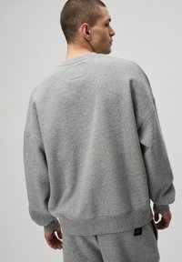 Szary sweatshirt o luźnym kroju, okrągłym dekolcie i długich rękawach. Wykonany z miękkiego materiału, z małą metką z logo na dole.