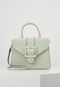 Tyrkysová kožená kabelka se strukturovaným designem, zlatými akcenty a průhlednou sponou. Má horní držadlo a odnímatelný ramenní popruh.