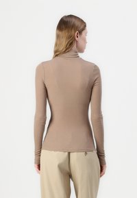Langermet, tettsittende turtleneck i ribbet, beige stoff. Har høy hals og smale ermer, kombinert med lyse bukser.