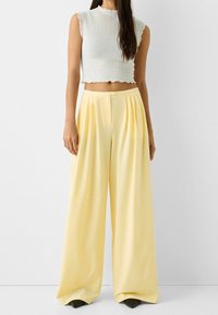 Cropped white smocked top with frilled hem paired with high-waisted yellow wide-leg pants featuring pleats and a button closure.
