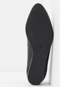 Semelle de chaussure noire avec motif antidérapant texturé et numéro de taille 37 visible, positionnée verticalement sur un fond blanc.