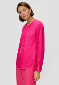 Langarmbluse aus lebhaftem pinkem Satin, mit rundem Ausschnitt, dezentem Knopfdetails und einem leicht gerundeten Saum.