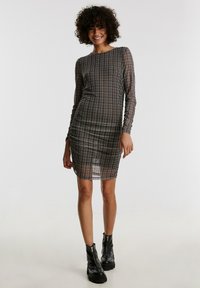 Durchsichtiges schwarzes Karo-Kleid mit langen Ärmeln; geraffte Details; figurbetonte Passform; kombiniert mit schwarzen Stiefeln mit dicker Sohle.