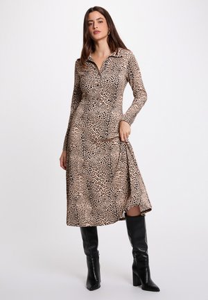 Langere jurk met lange mouwen en kraag, bedrukt met luipaardprint, voorzien van een aansluitend lijfje en een uitlopende rok. Gecombineerd met zwarte kniehoge laarzen met hak.