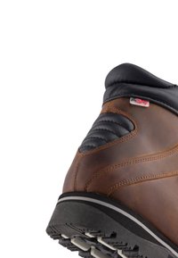 Hnědá kožená bota s černým polstrovaným límcem, texturovanými bočními akcenty a robustní gumovou podrážkou s výrazným vzorem. 