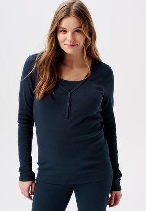 Navy blauwe, lange mouw ribbeltop met een ronde halslijn en een knoopsluiting. Gecombineerd met bijpassende onderkant, met een gladde textuur.
