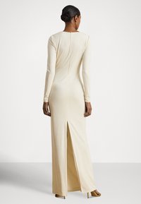 Vestido creme de manga comprida feito de tecido liso, com fecho de correr nas costas e uma fenda alta na bainha para facilitar os movimentos.