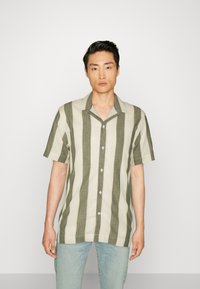 Camisa de manga corta abotonada de tejido a rayas verde oliva y crema; diseño ligero, con cuello y un corte relajado, y botones visibles.