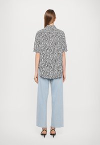 Black and white short-sleeve shirt with a spotted pattern, paired with light blue wide-leg jeans and black strappy sandals.