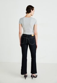 Mørke denim flared jeans med kontrastsøm, fem pocket-design og et lædermærke på bagsiden, parret med en grå tætsiddende t-shirt.