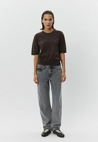 Brown short-sleeve knit top paired with light gray wide-leg jeans and black slip-on shoes with white accents and studs.