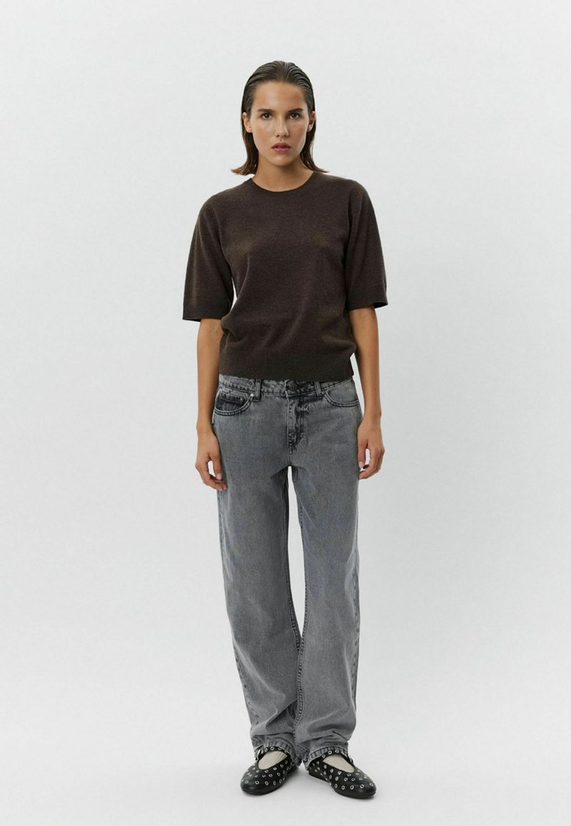 Brown short-sleeve knit top paired with light gray wide-leg jeans and black slip-on shoes with white accents and studs.