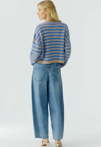 Gestreepte cropped trui in blauw en tan, gecombineerd met lichtblauwe wijde broekspijpen. De trui heeft een losse pasvorm en een zachte textuur.