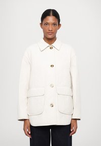 Quilted cream jacket with a collar, four buttons, and two front pockets. Features a smooth texture and a relaxed fit.