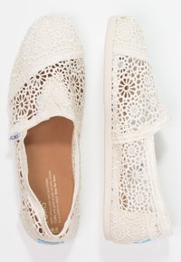 Chaussures beige en dentelle à enfiler avec motif floral et dessus en textile, dotées d'une semelle intérieure rembourrée et de côtés élastiqués pour un enfilage facile.