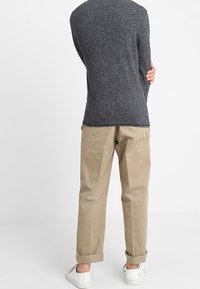Pull à manches longues gris foncé texturé, associé à un pantalon beige retroussé aux chevilles et des baskets blanches, vu de dos.