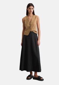 Top sans manches en lin marron avec des boutons, associé à une longue jupe noire et des sandales à glissière noires texturées. Design simple et minimaliste.